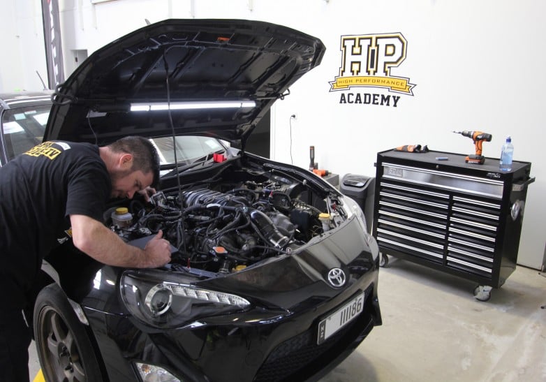 mechanic diagnosing tuning fault over open engine bay