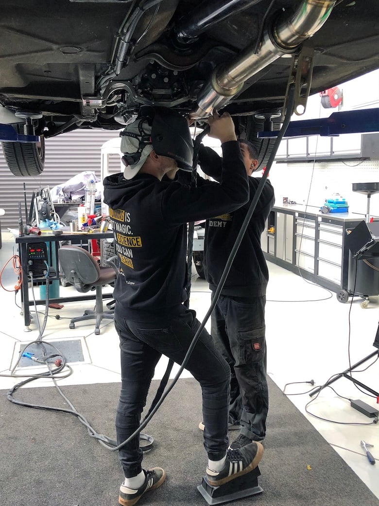 High Performance Academy team modifying the Volvo 240 exhaust beneath the car for ZF 8HP clearance.